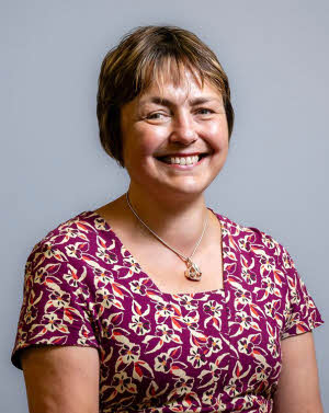 A seated Dr Jane Povey in three-quarter view, smiling at the camera