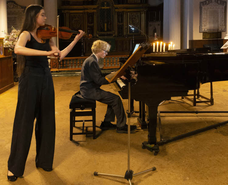 Una stands playing the violin whilst Edward is seated playing the piano